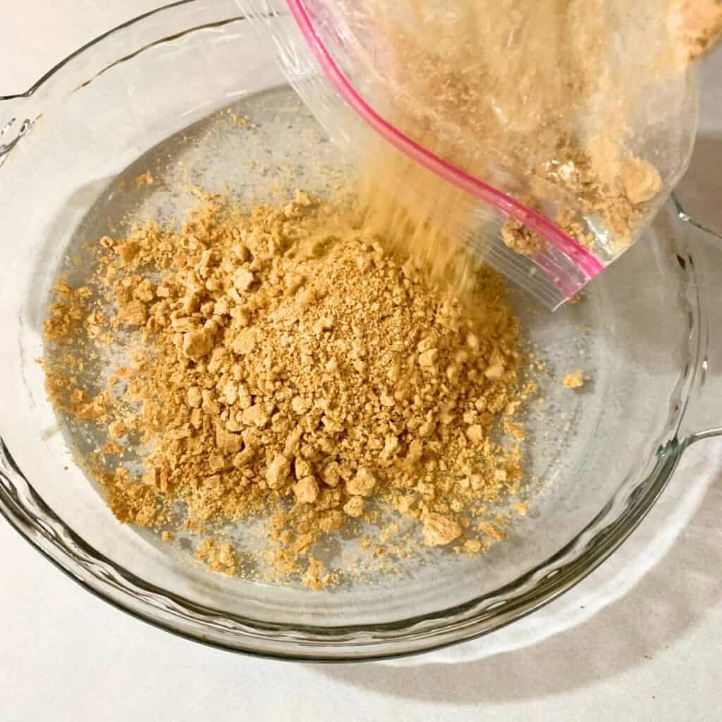 Woman pouring graham cracker crumbs into a glass pie dish.