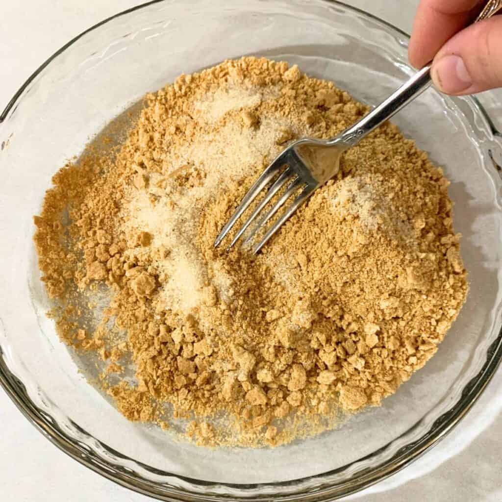 Woman mixing sugar with graham cracker crumbs using a fork.