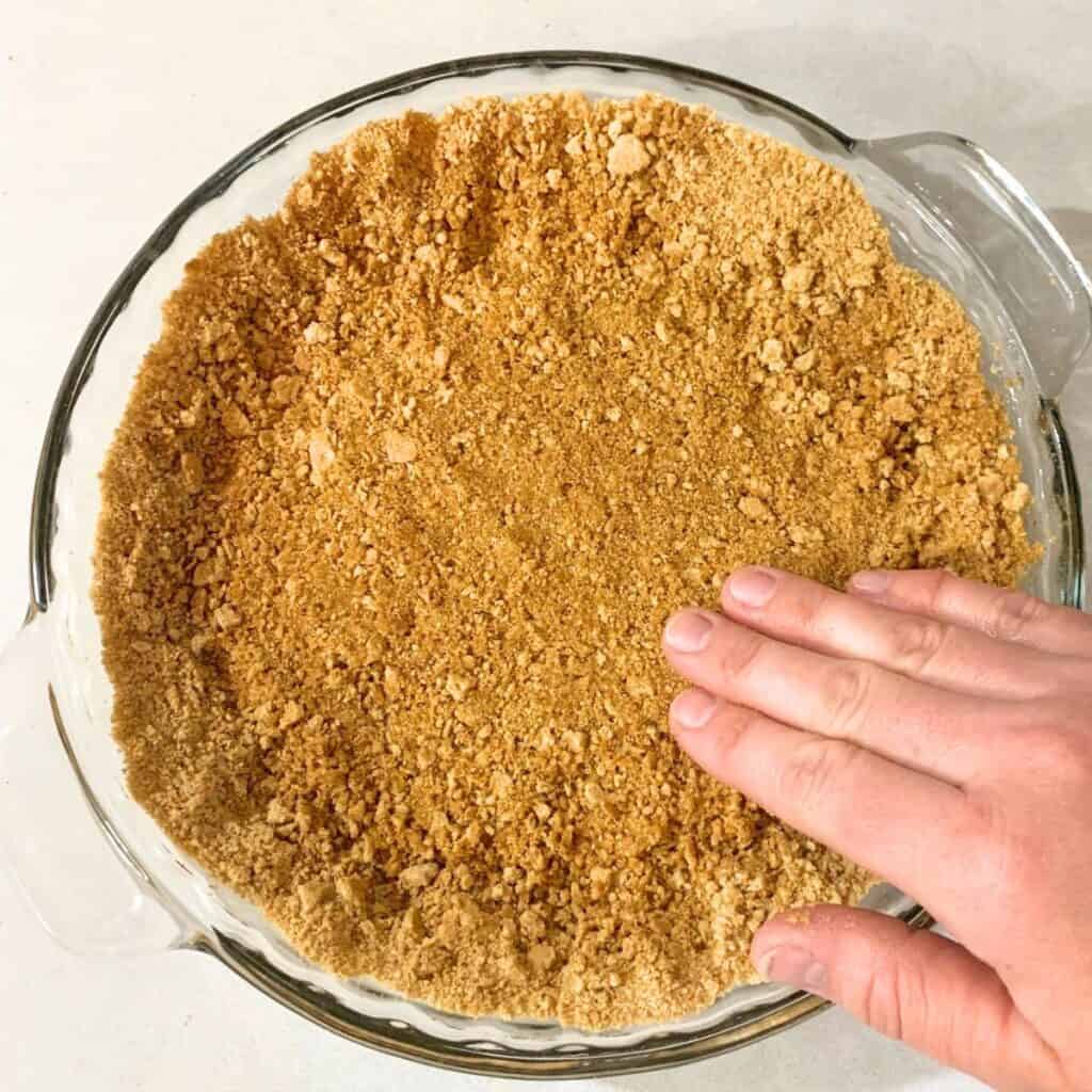 Woman pressing graham cracker crumbs in a glass pie dish.