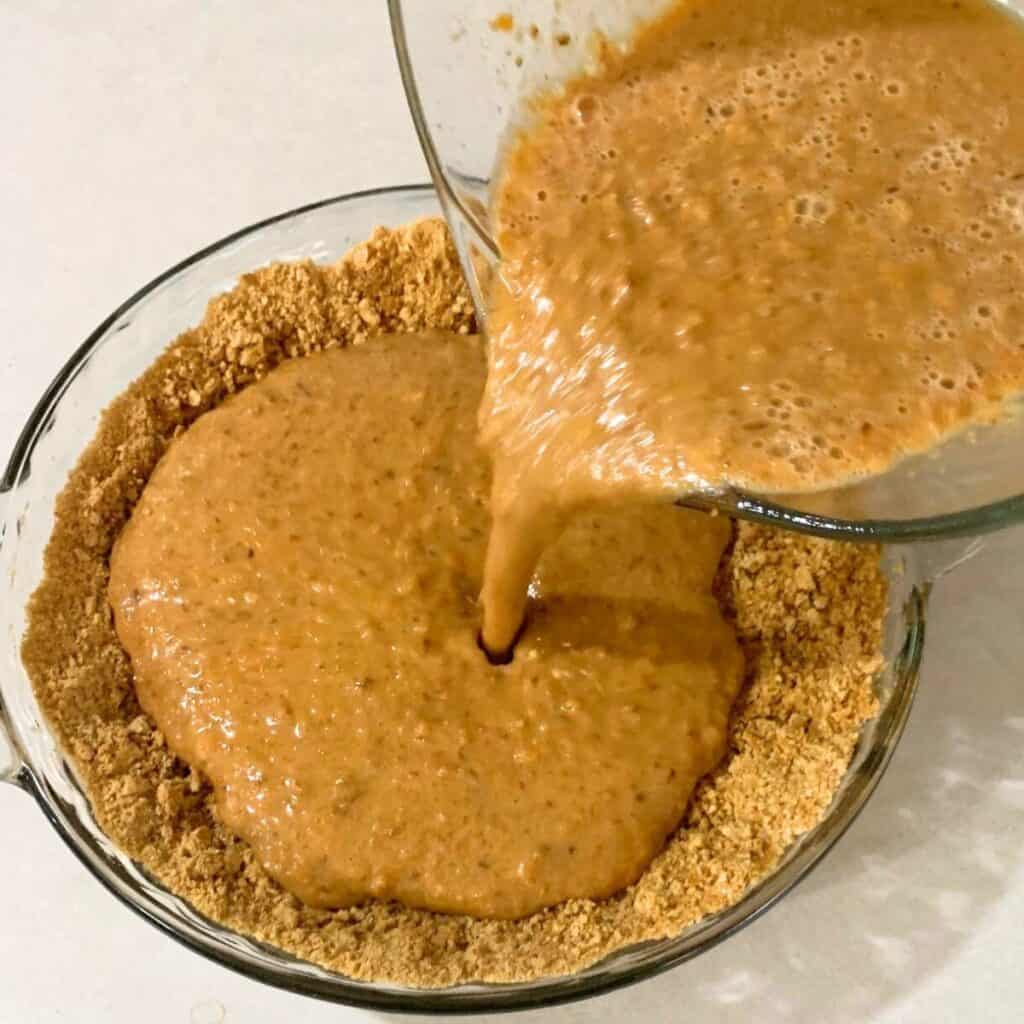 Woman pouring carrot pie filling into a pie dish with graham cracker crust.