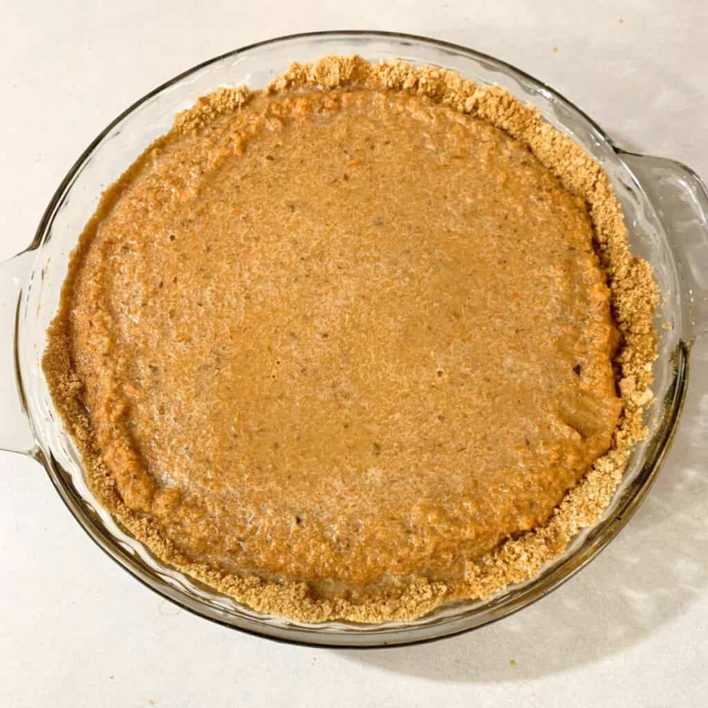 Uncooked carrot pie filling in a graham cracker pie crust on the stove.