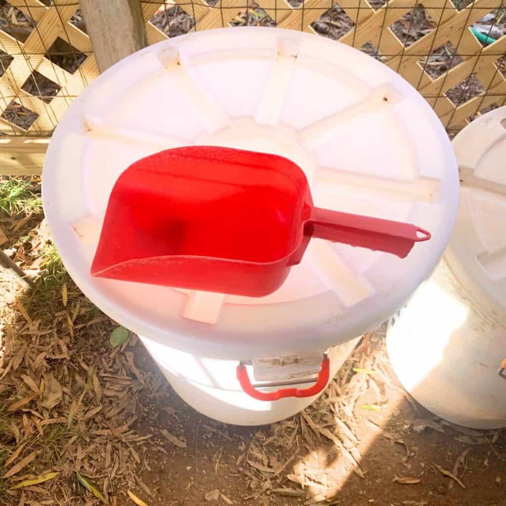 A white storage bin with lid and a red utility scoop sitting on top.