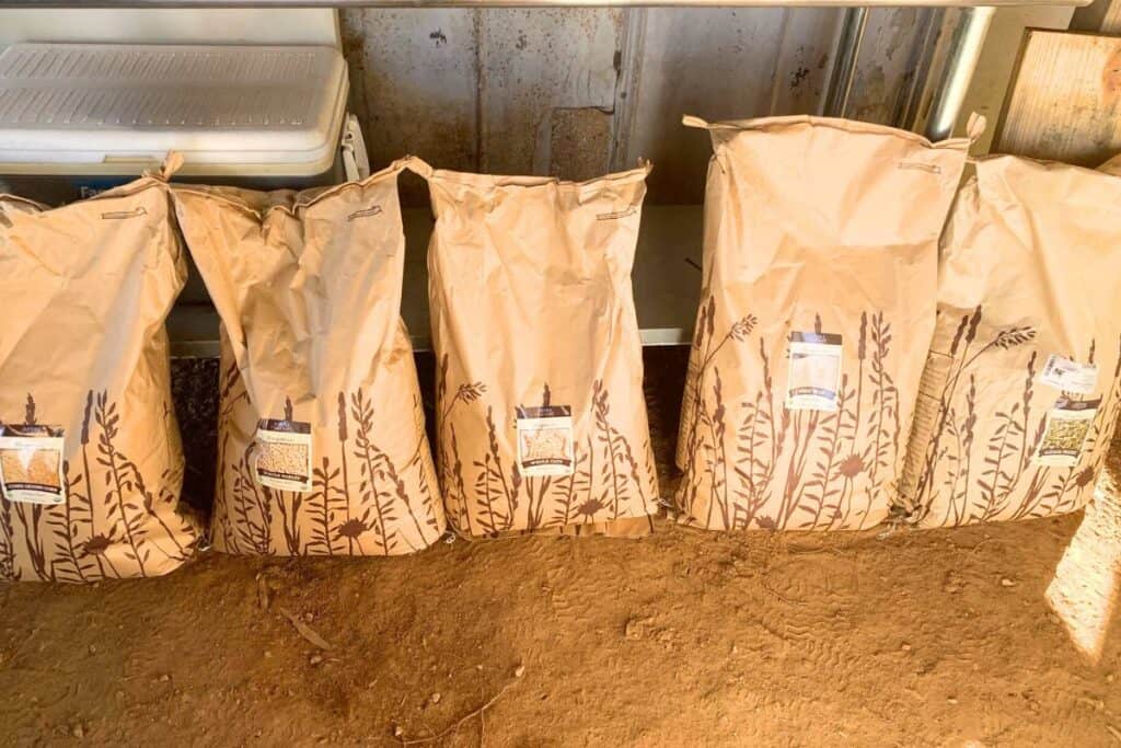 Bags of organic feed for dairy cows including cracked corn, barley, oats, wheat bran, and alfalfa pellets.