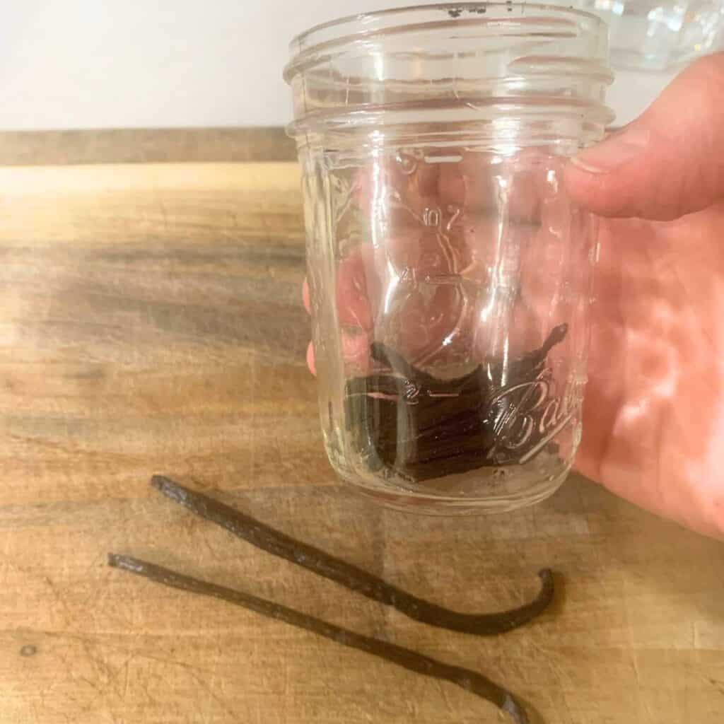 Woman holding a half pint mason jar of cut vanilla beans.