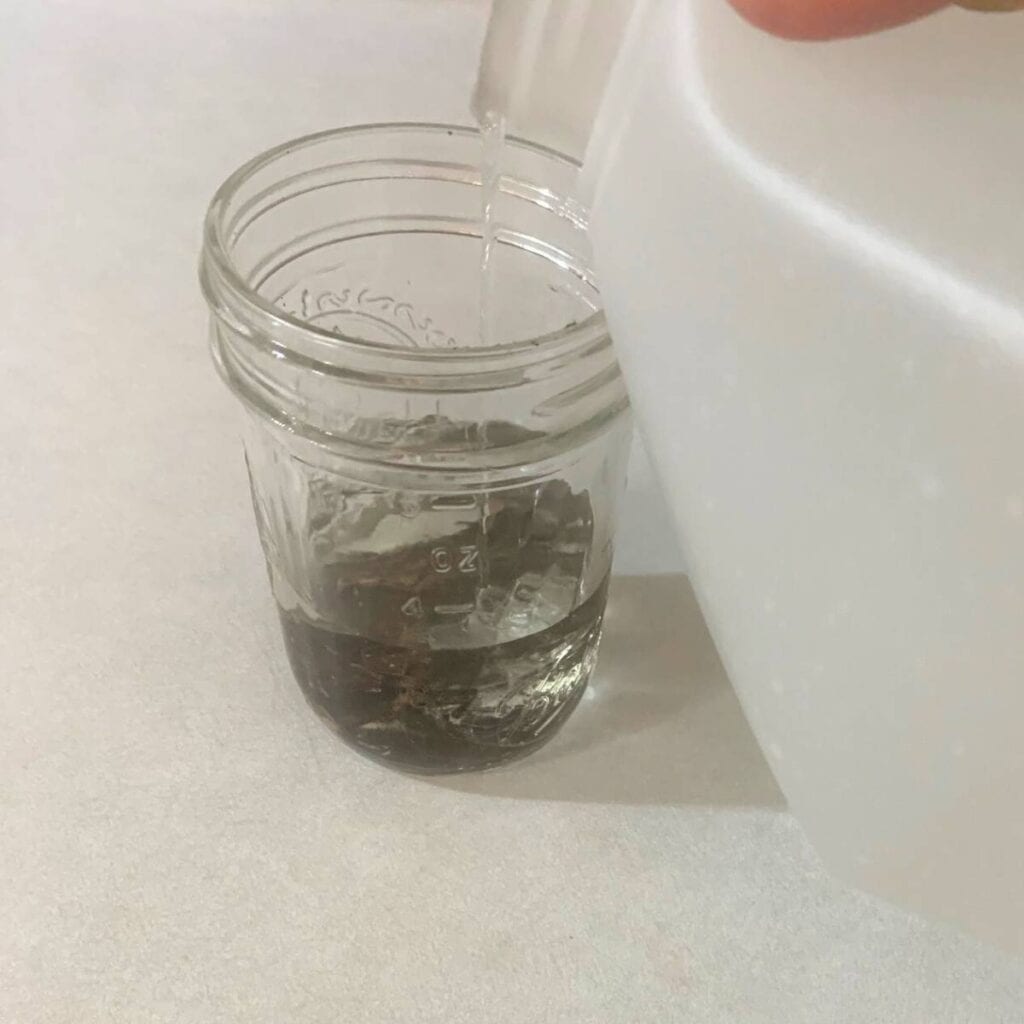 Woman pouring non-GMO vegetable glycerin into a mason jar with water and vanilla beans. 