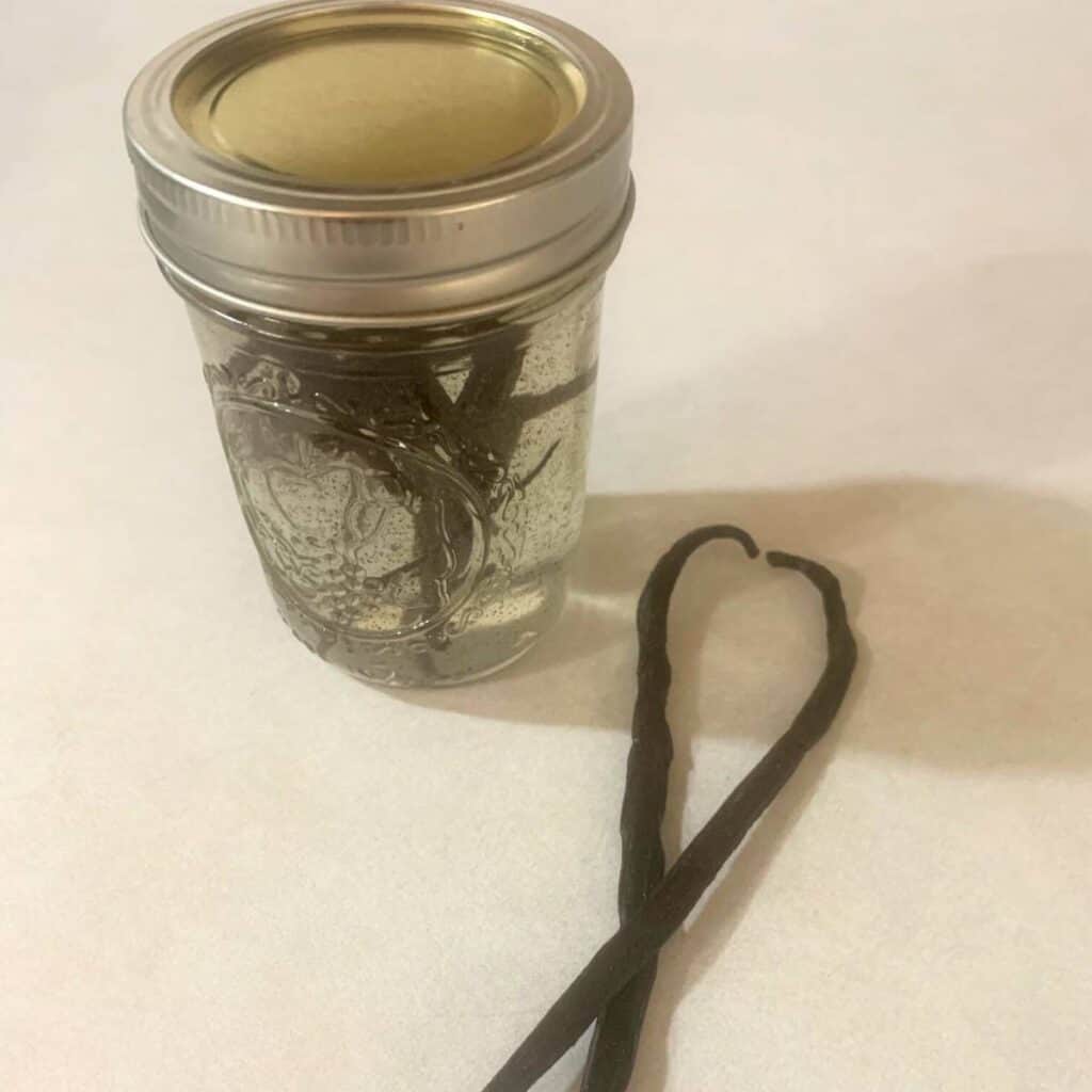 Glass jar of alcohol free vanilla extract sitting on a kitchen counter next to two vanilla beans.