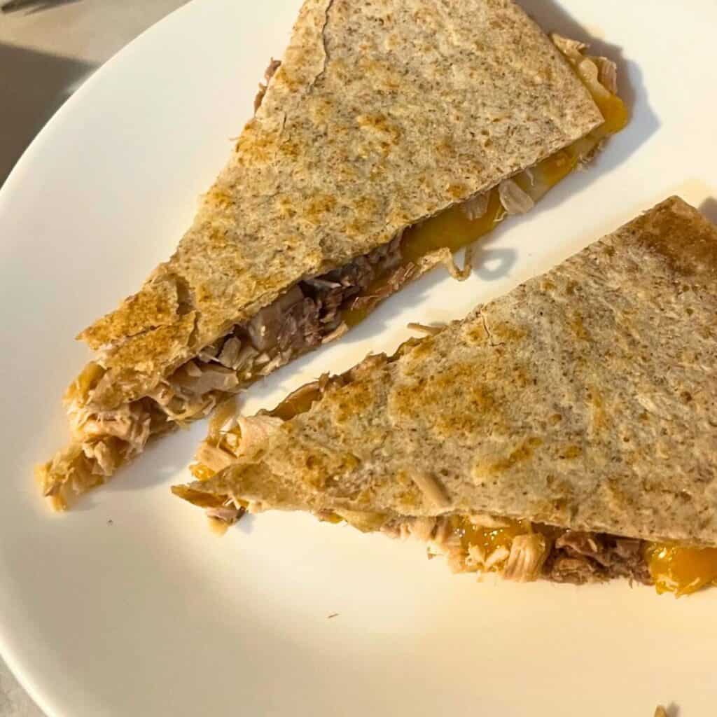 Two wedge slices of chicken and cheese quesadilla on a white plate.