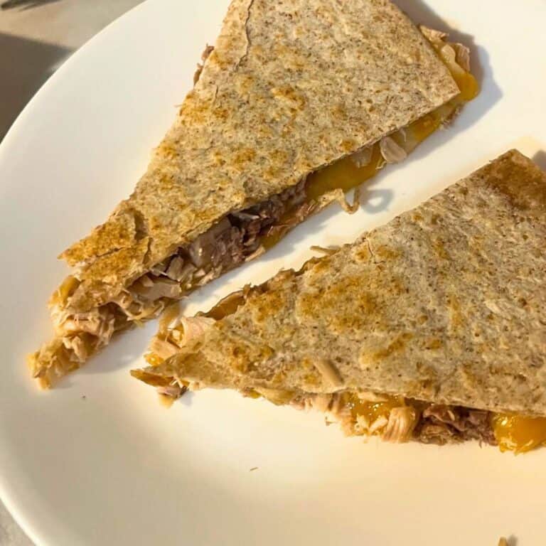 Two wedge slices of chicken and cheese quesadilla on a white plate.