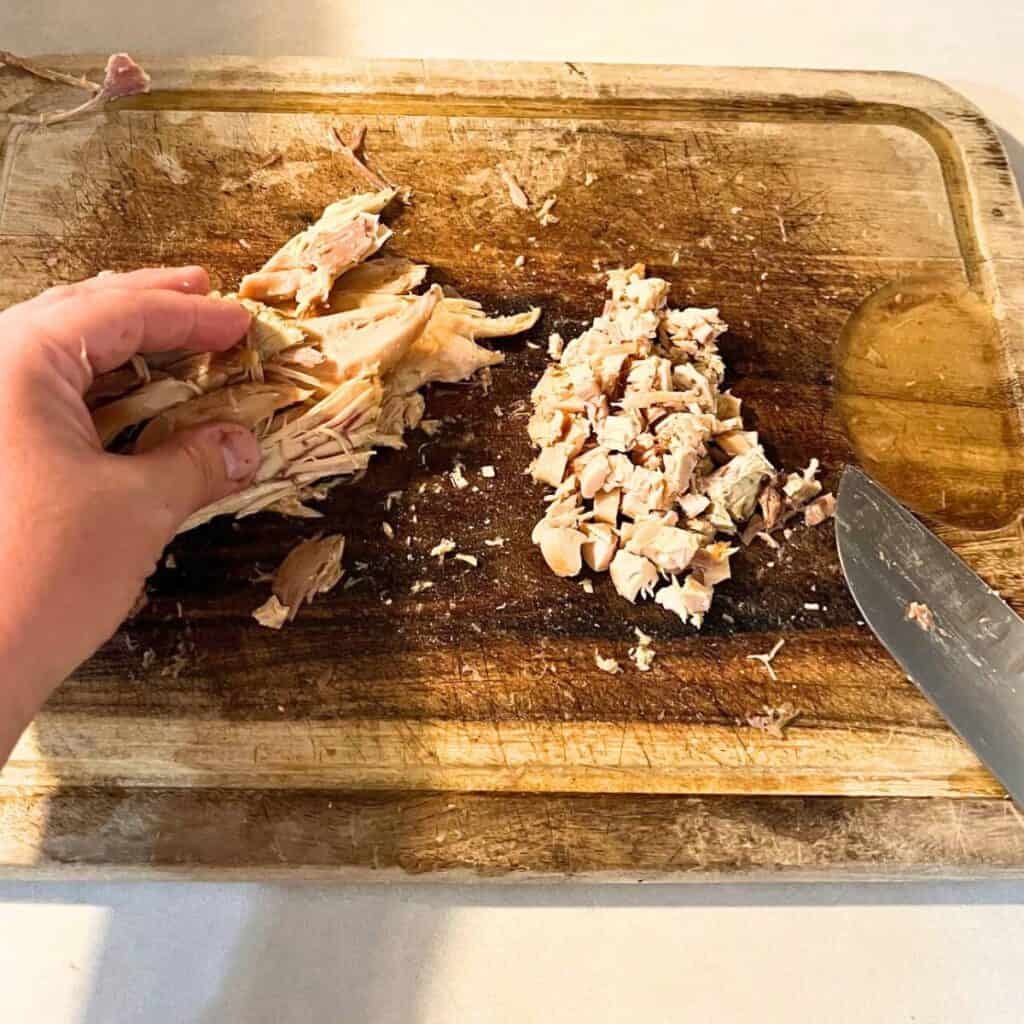 Woman cutting chicken into pieces on a wooden cutting board.