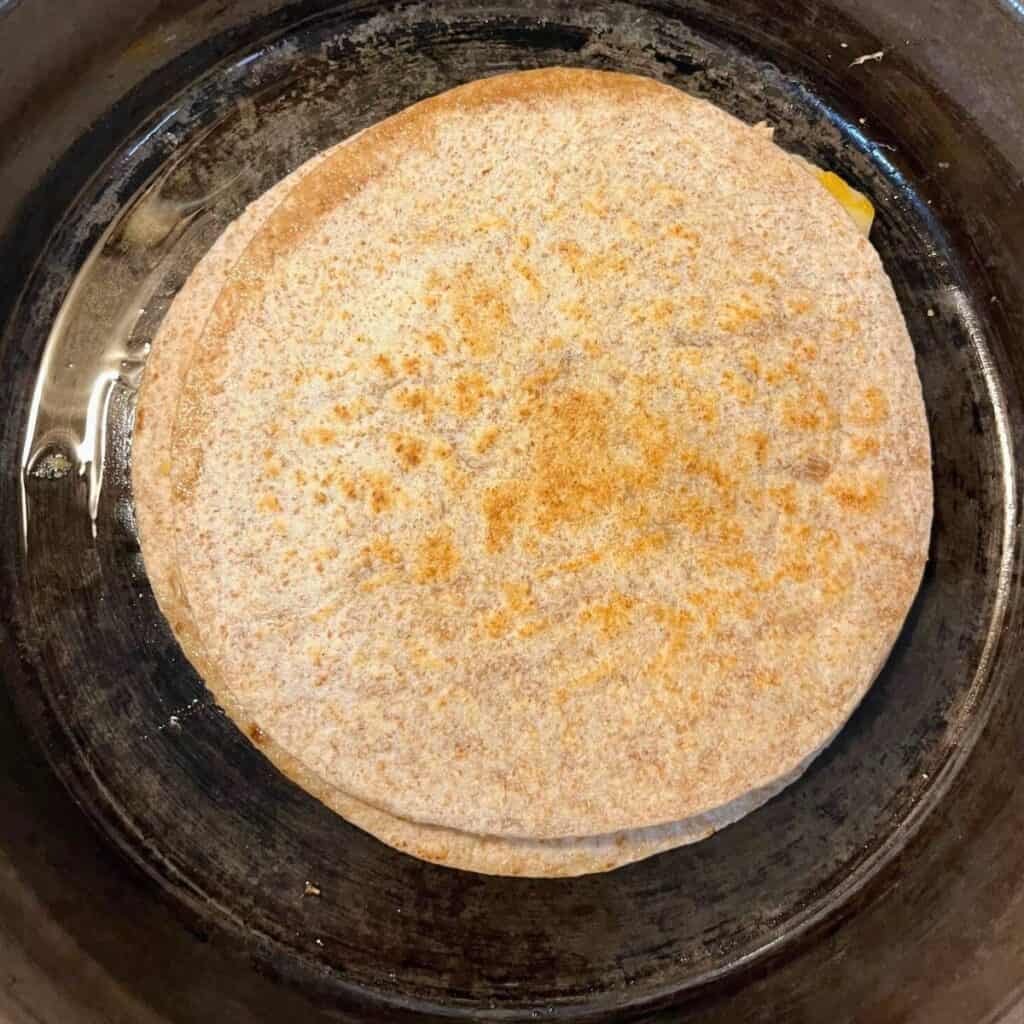 A golden brown tortilla-topped chicken and cheese quesadilla in a cast iron skillet.