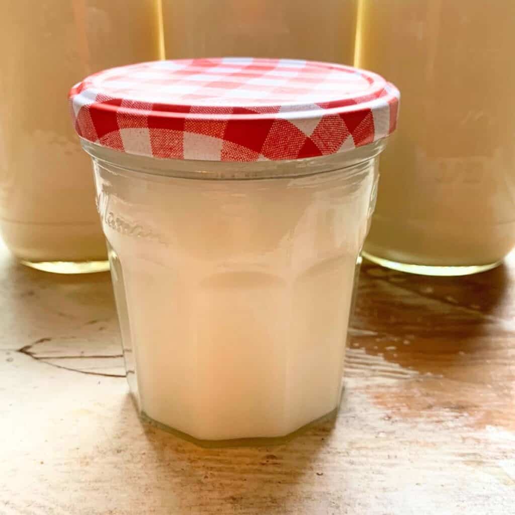 A small glass jar of home-rendered lard sitting in front of three larger jars on a white table.