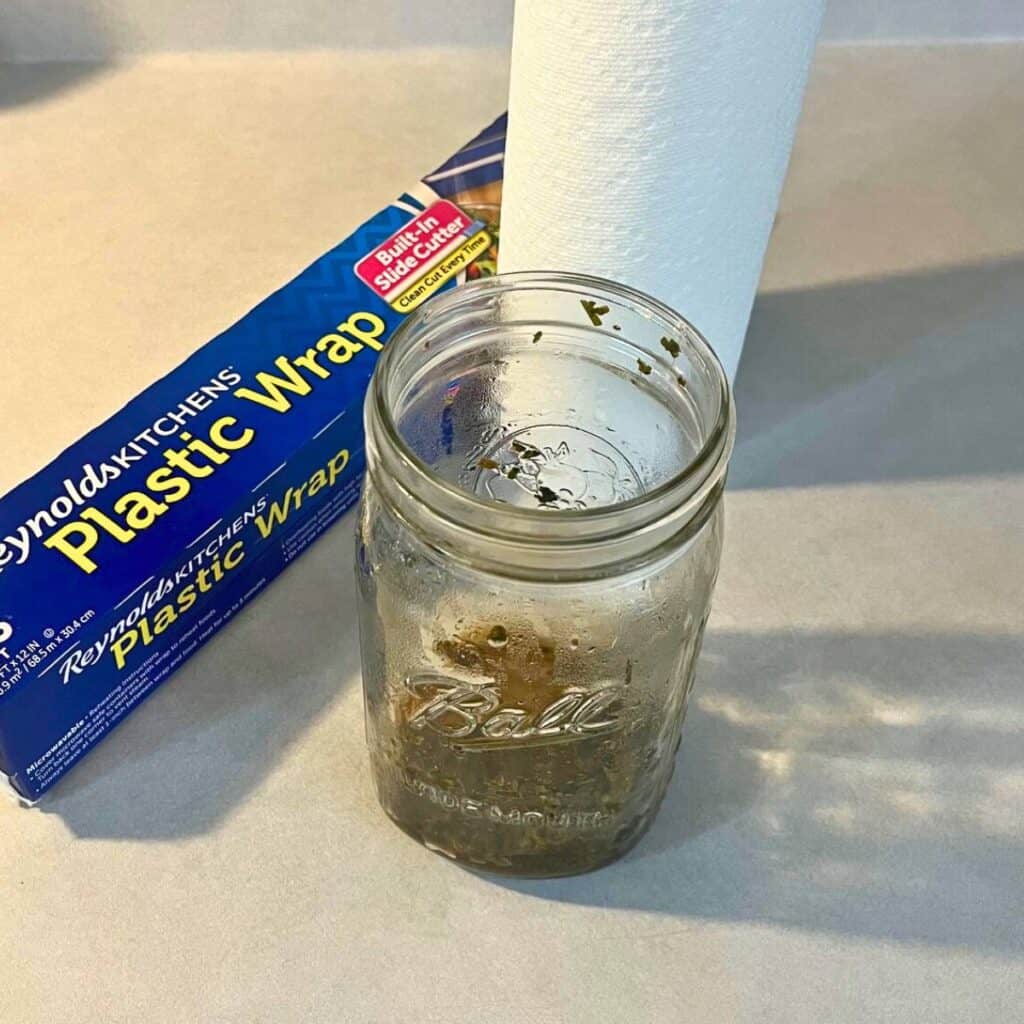 A box of plastic wrap, a glass jar of blended comfrey leaves, and a roll of paper towels on a kitchen counter.