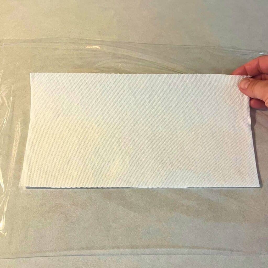 Woman putting paper towels down onto plastic wrap on a kitchen counter.
