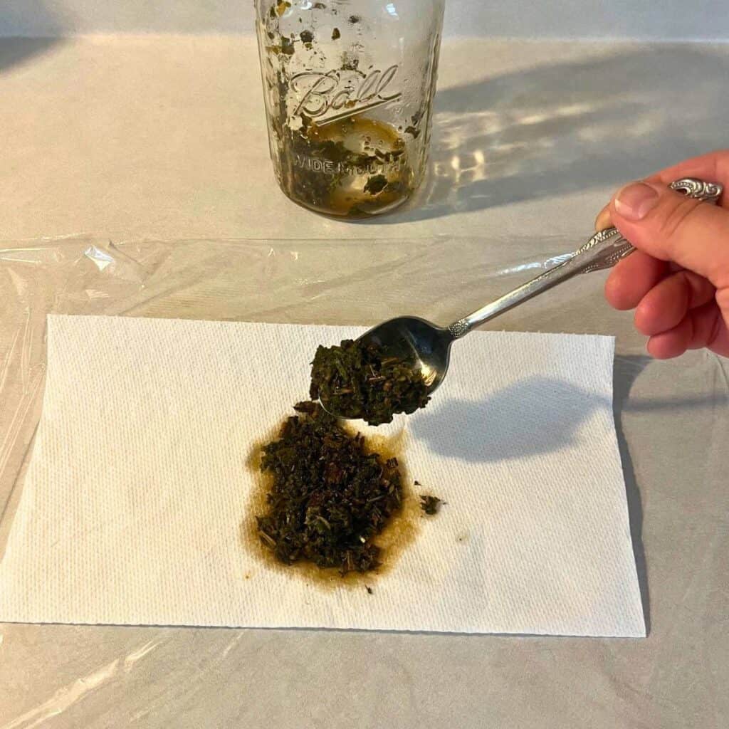 Woman adding comfrey paste onto paper towels sitting on plastic wrap.