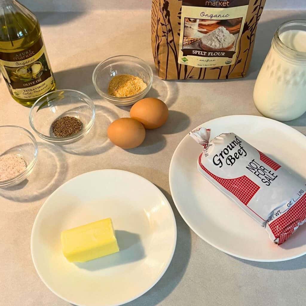 Ingredients to make country fried steak including flour, milk, ground beef, butter, salt, pepper, seasoned salt, eggs, and olive oil.