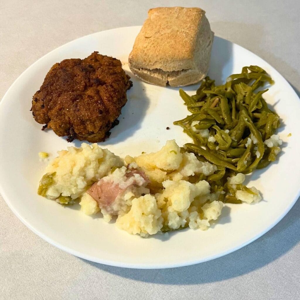 Country fried steak, mashed potatoes, green beans, and a biscuits on a white plate.