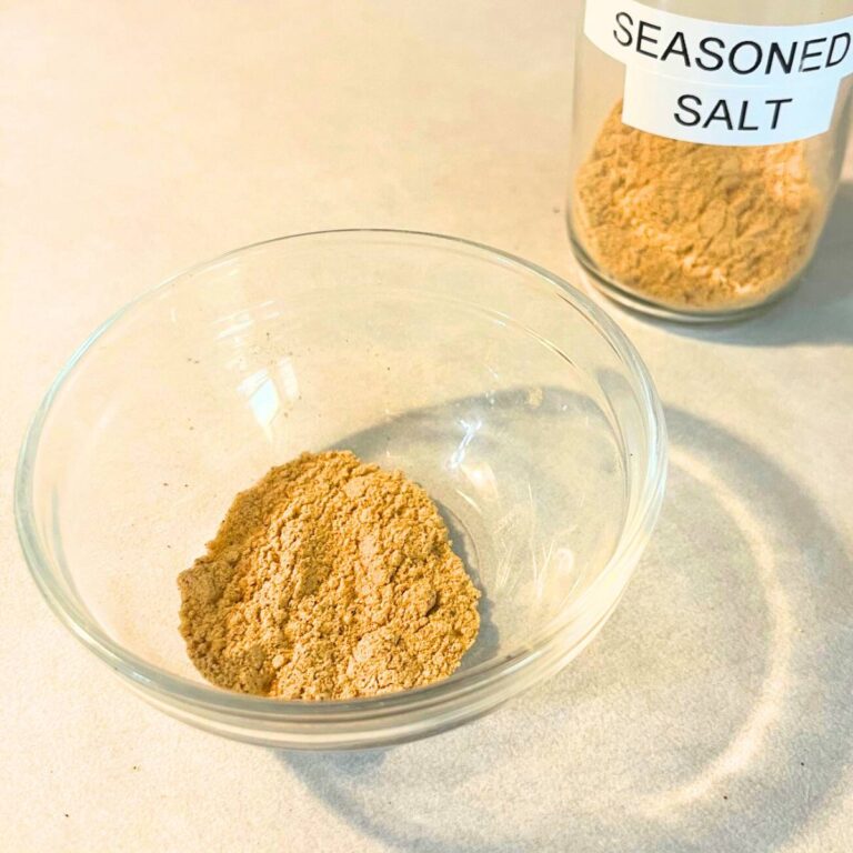 A bowl of homemade seasoned salt sitting on a kitchen counter next to a small glass jar of seasoned salt.