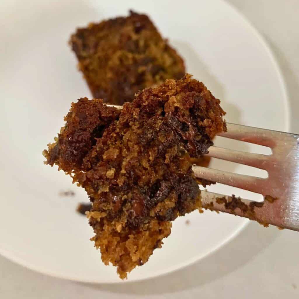 Woman cutting a piece of chocolate banana bread on a white plate with a silver fork.