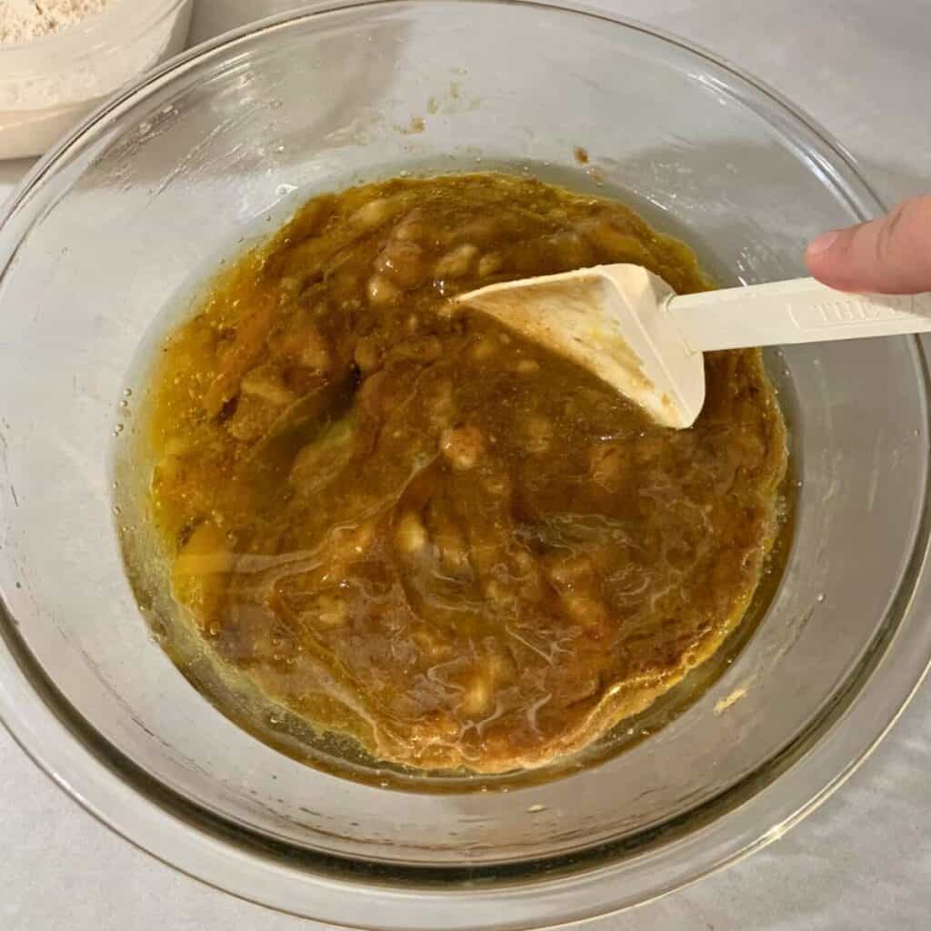 Woman mixing ingredients in a glass bowl with a white rubber spatula.