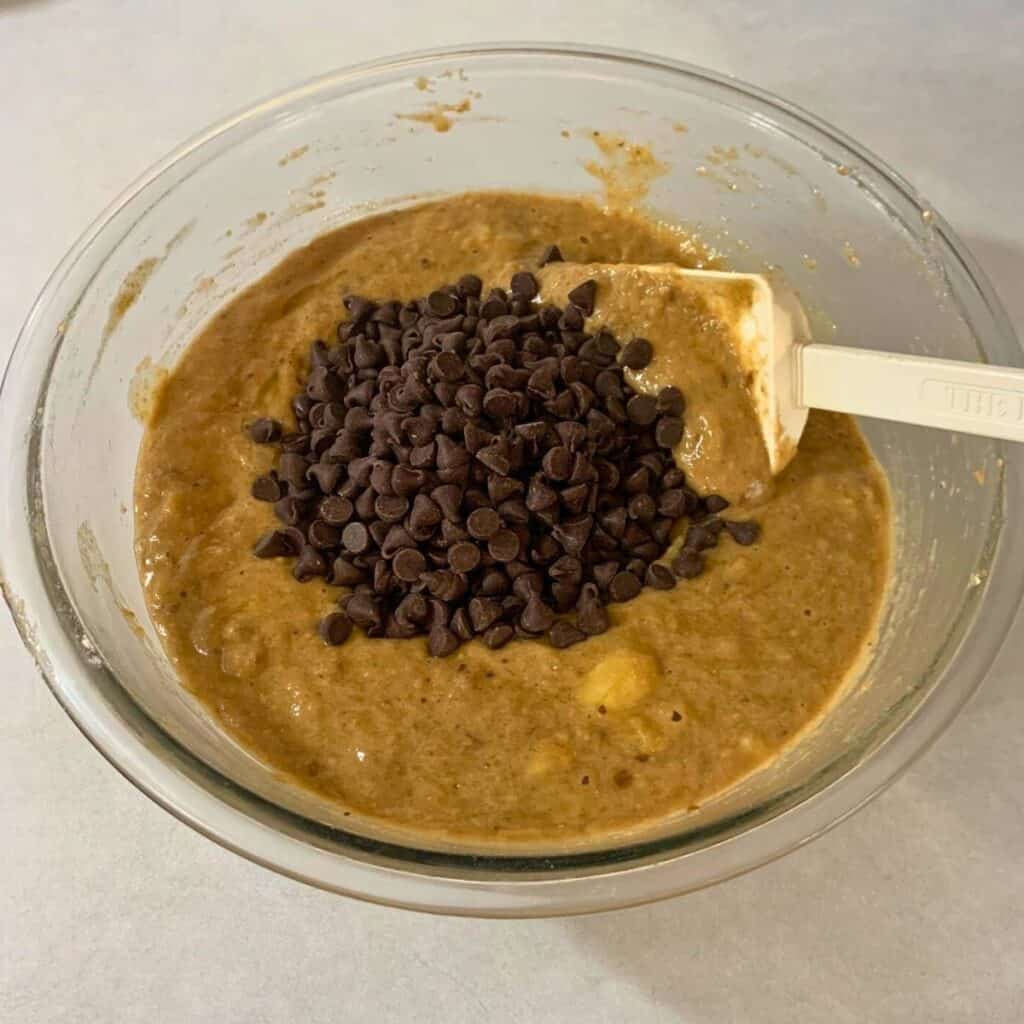 Woman stirring in chocolate chips into chocolate banana bread batter in a glass mixing bowl.