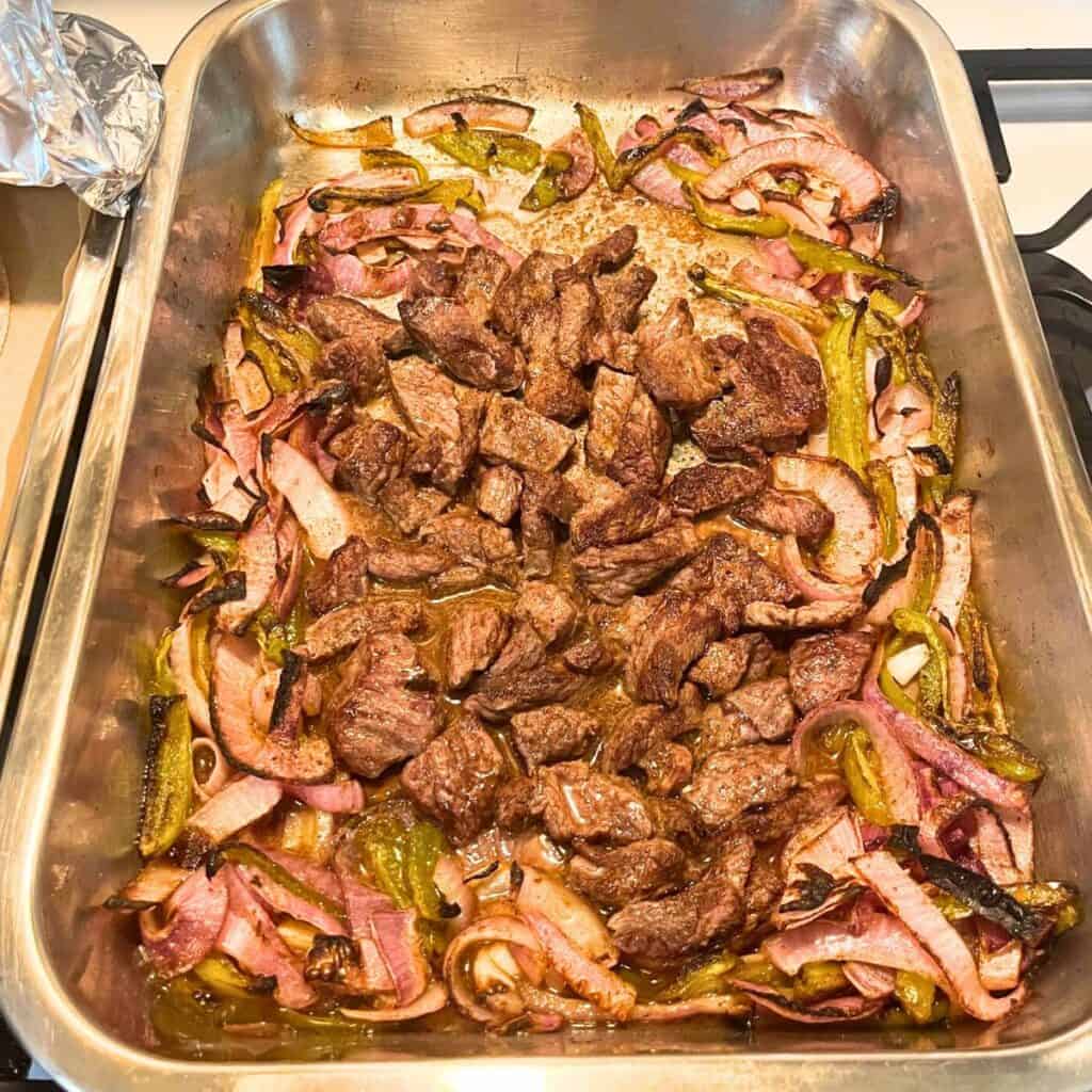 Steak fajita in one pan shows sliced onions, peppers, and steak in one oven pan.