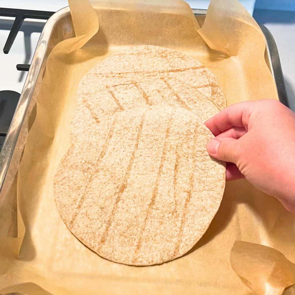 Woman placing flour tortillas in the bottom of a parchment-lined lasagna pan.