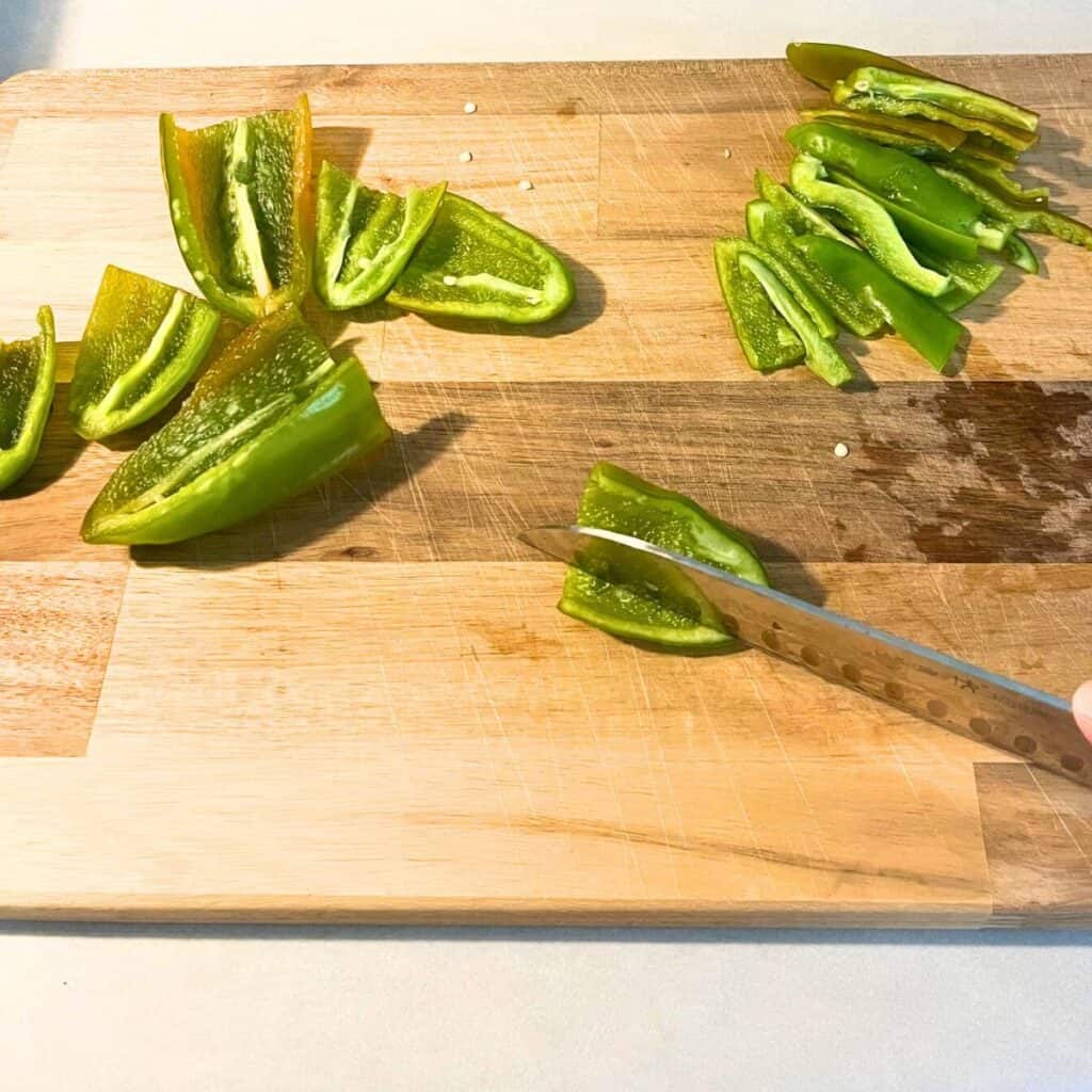Woman slicing green banana peppers on a wooden cutting board.