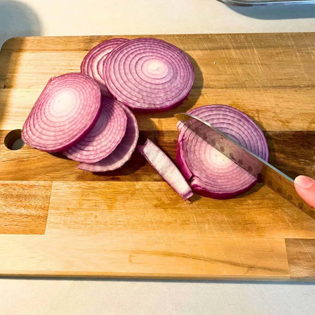 Woman slicing a red onion on a wood cutting board.