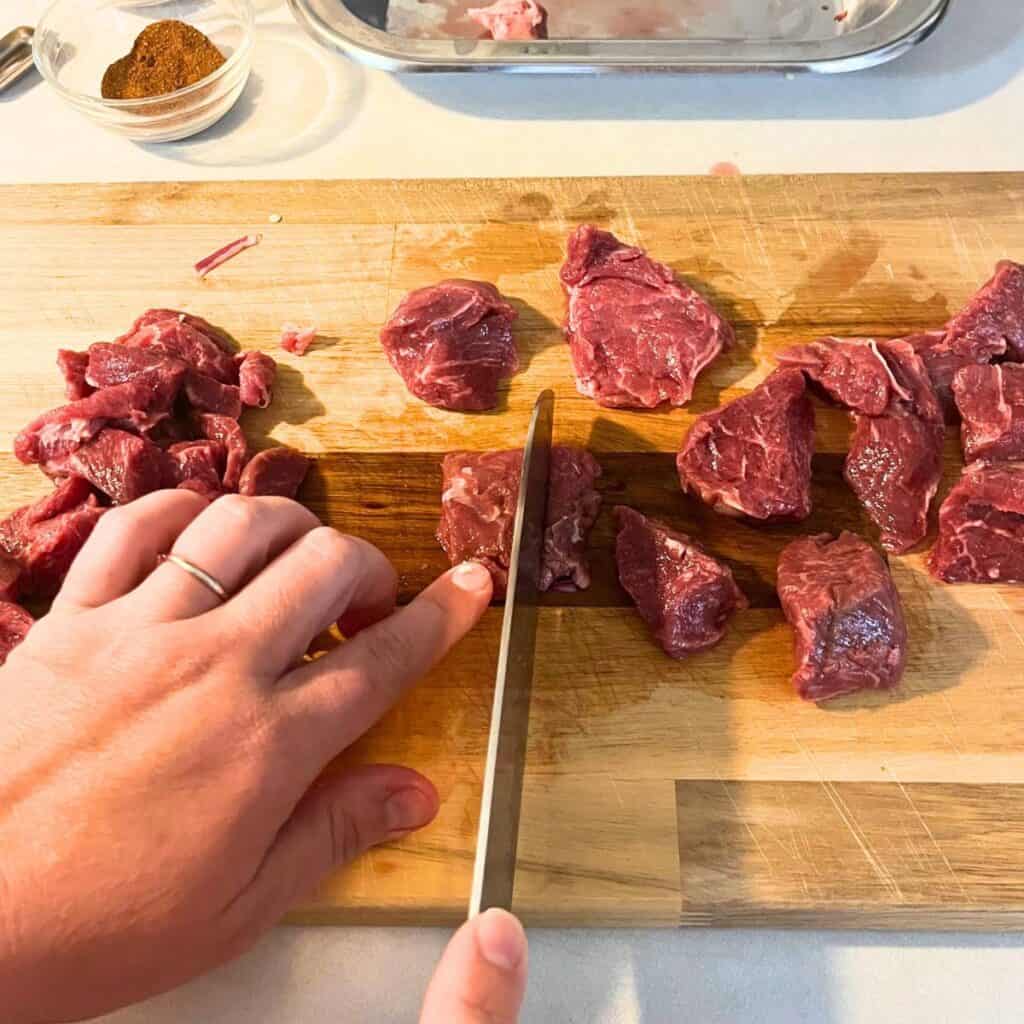Woman slicing beef stew meat on a wood cutting board.