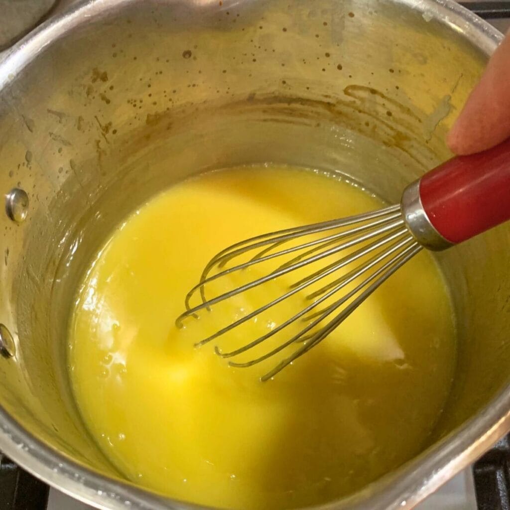 Woman whisking wet ingredients in a medium saucepan. 