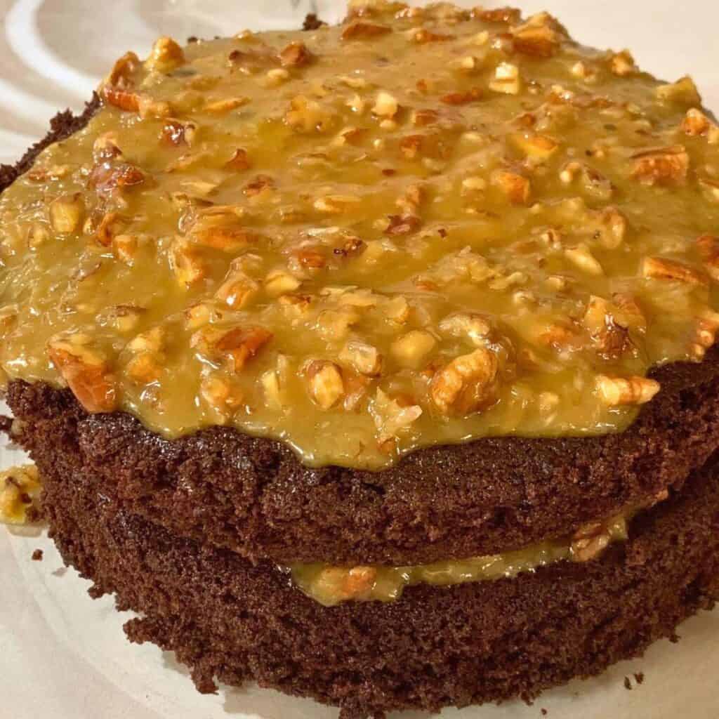 A two layer German chocolate cake with pecan and coconut icing on a glass cake plate.