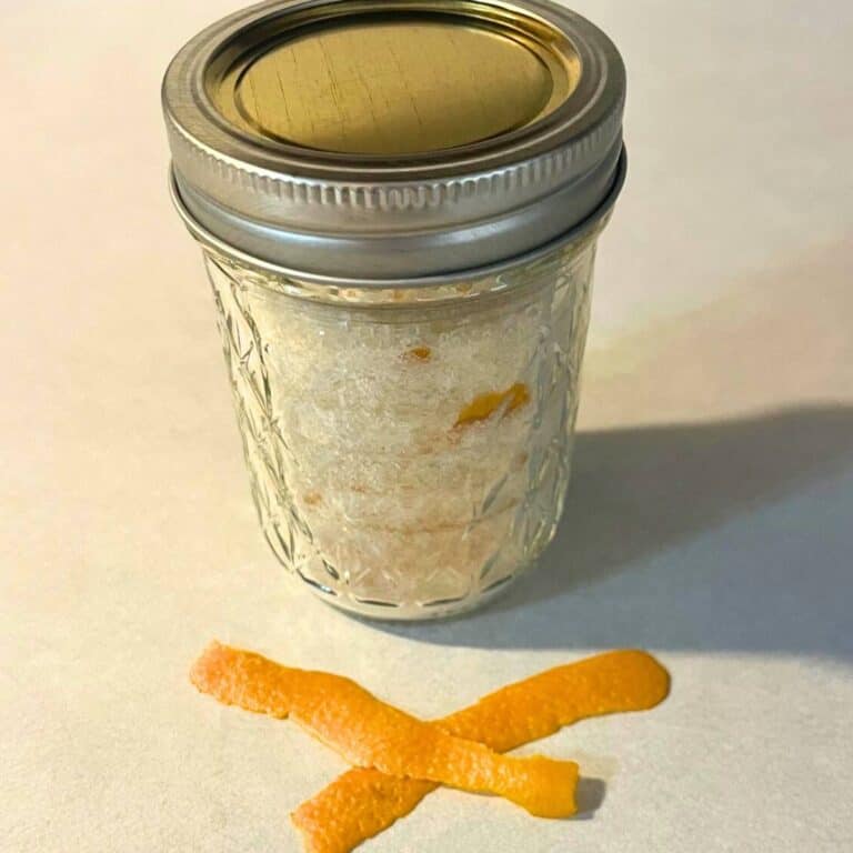 A glass mason jar of orange sugar sitting on a kitchen counter next to wide shreds of orange zest.
