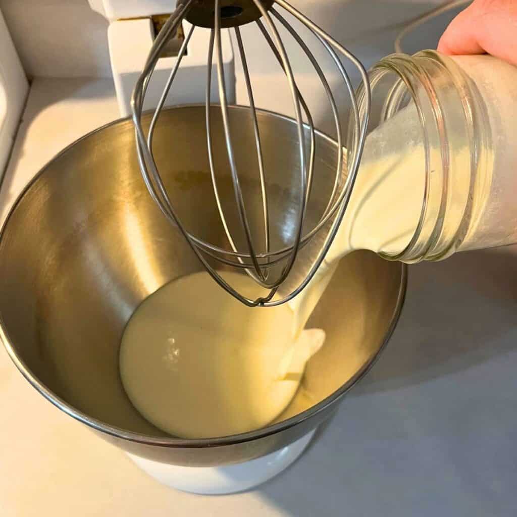 Woman pouring heavy cream into the bowl of a stand mixer with whisk attachment.