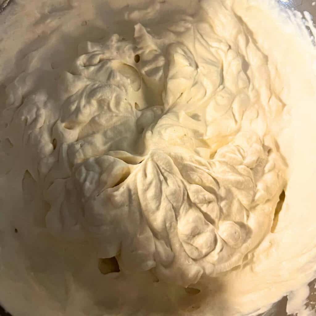 A stainless steel mixing bowl with homemade whipped cream showing soft peaks.