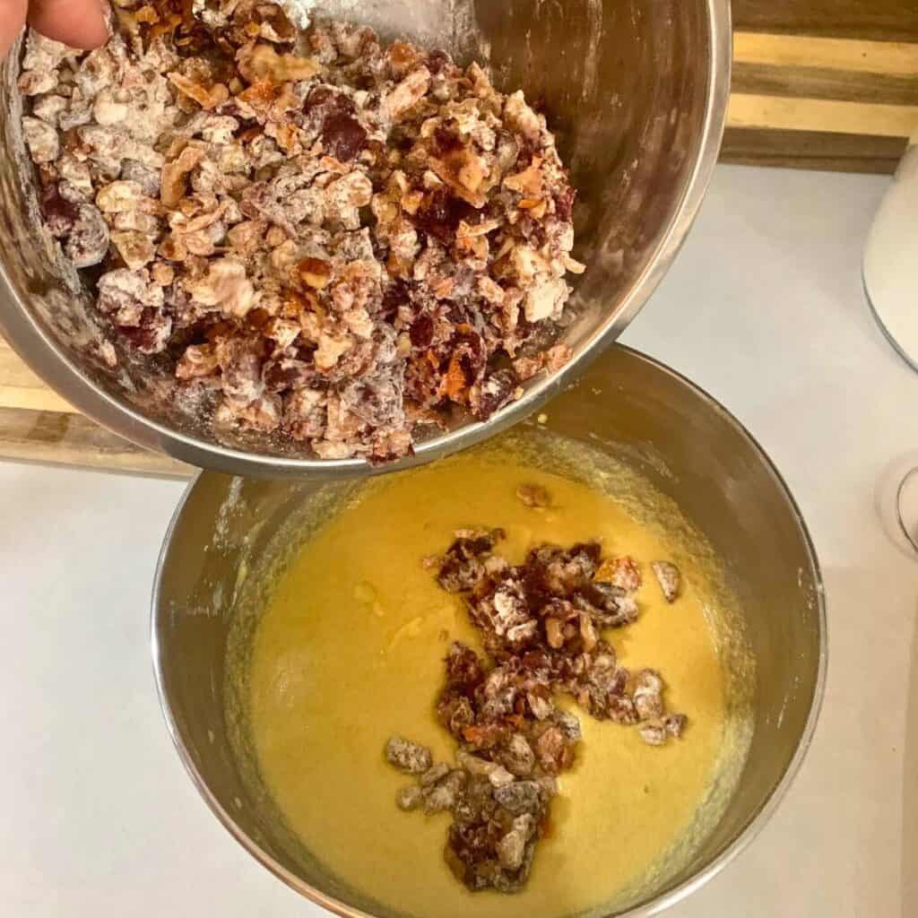 Woman adding floured nuts and fruit to fruit cake batter.