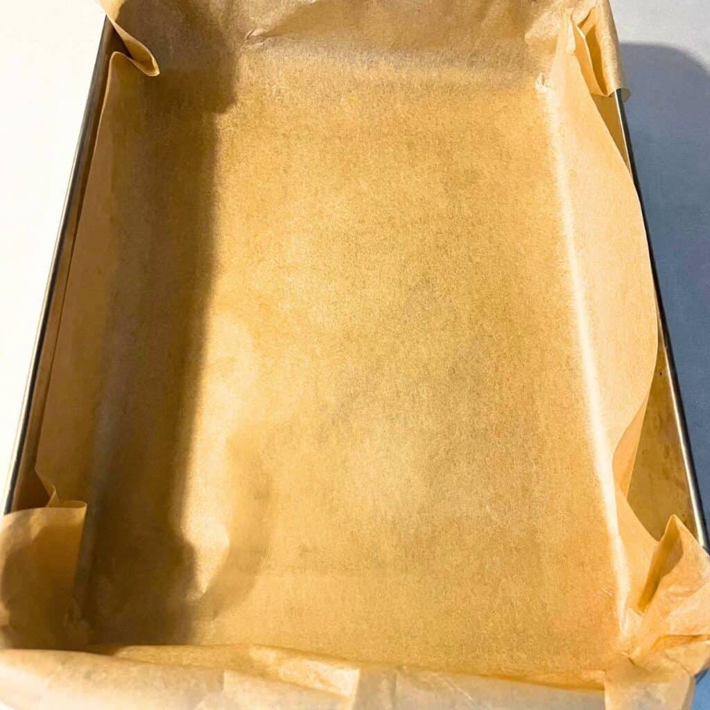 A 9x13 stainless steel pan lined with unbleached parchment paper sitting on a kitchen counter.