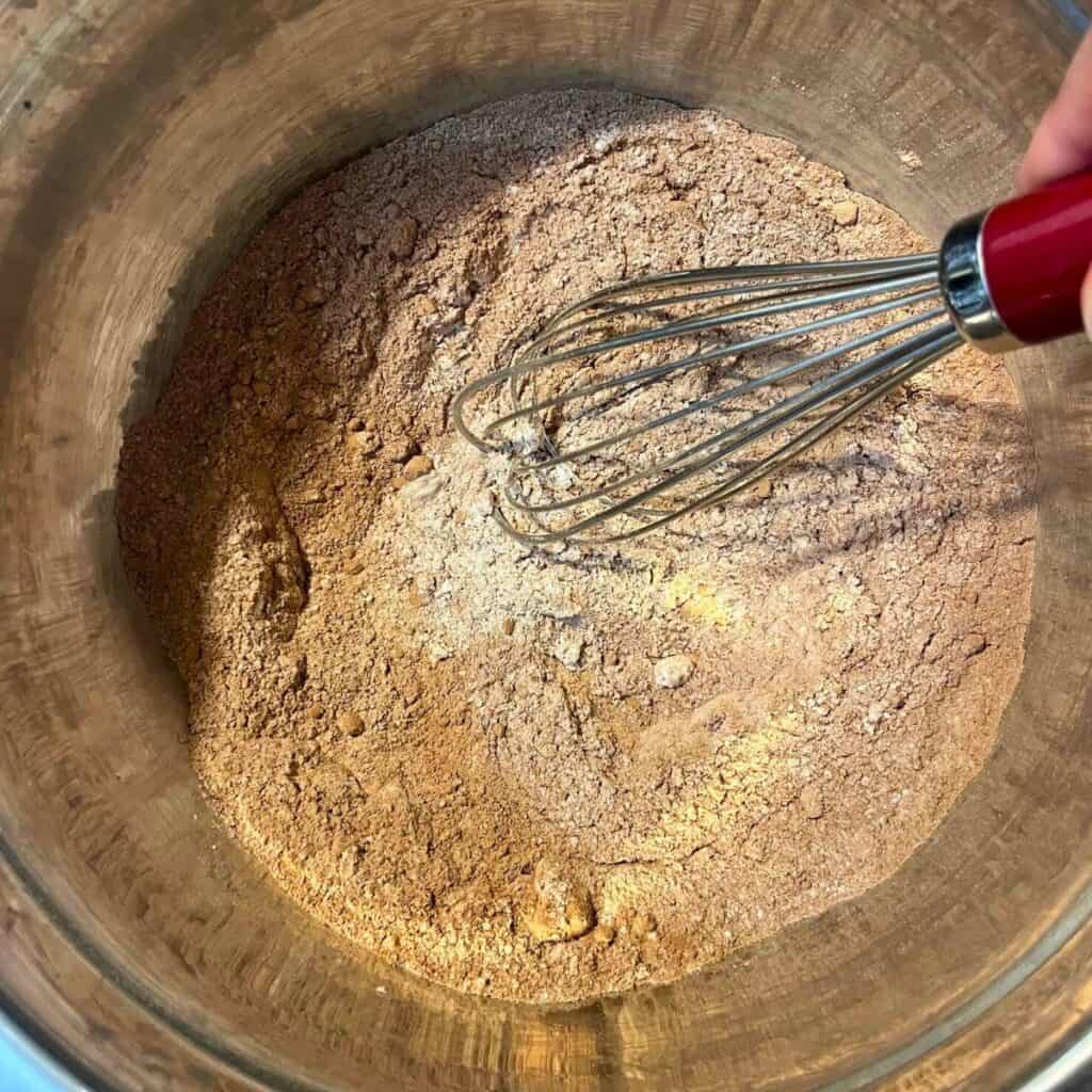 Woman whisking dry ingredients together in a stainless steel bowl with a wire whisk.