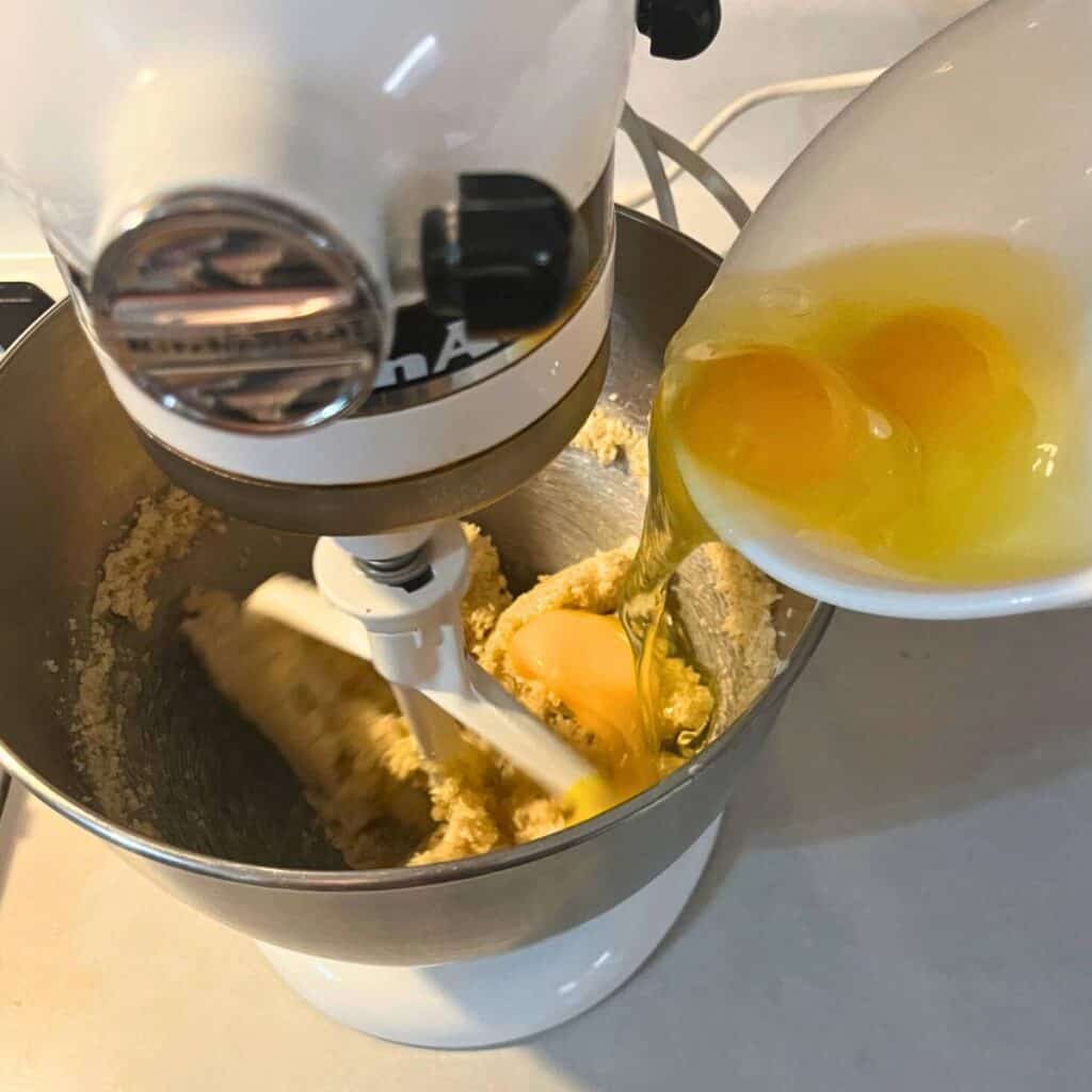 Woman adding eggs to the bowl of a stand mixer that has creamed butter and sugar.
