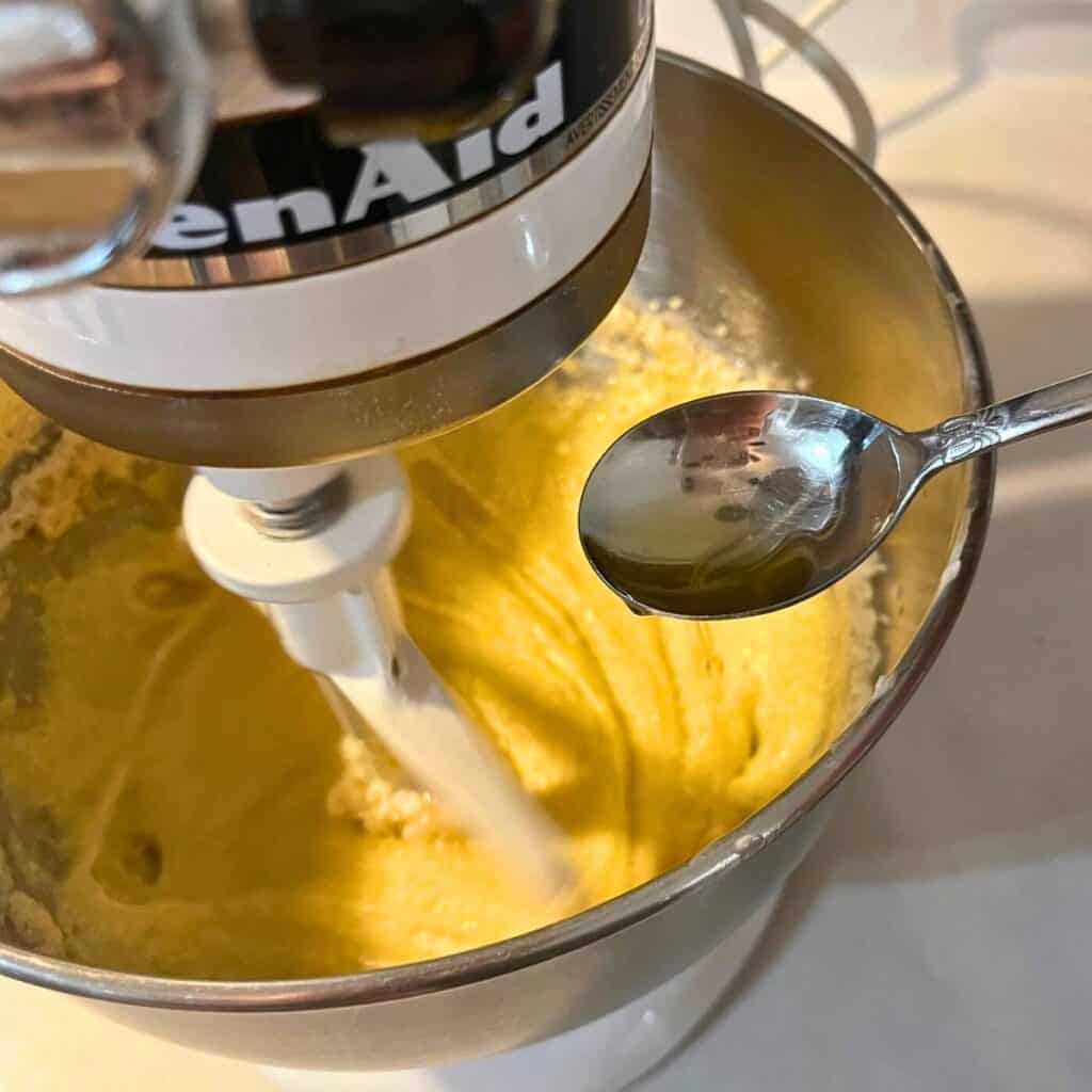 Woman adding vanilla extract to the bowl of a stand mixture with creamed sugar, butter, and eggs.