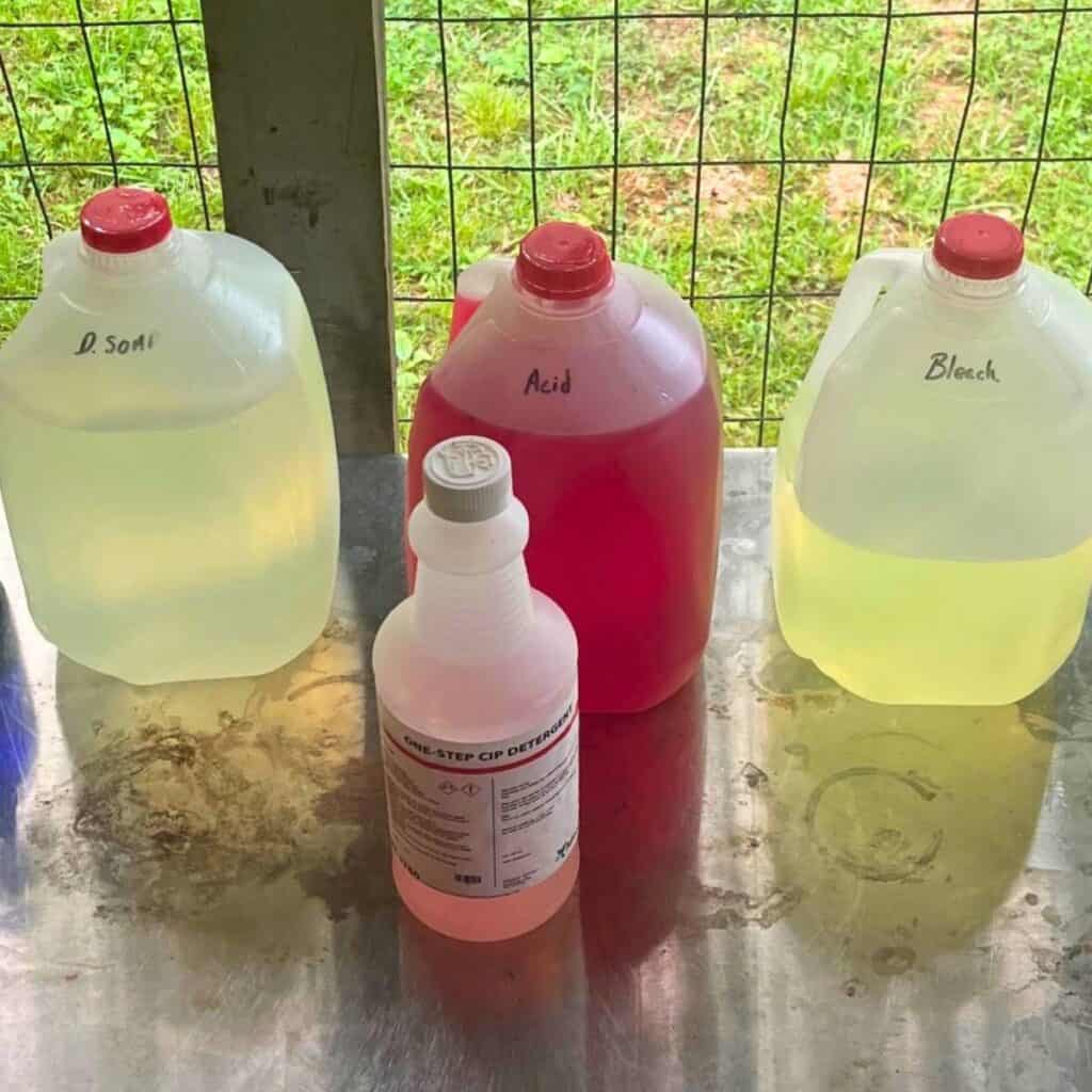 Gallon just of dairy soap, dairy acid, and dairy bleach sitting on a stainless steel table.