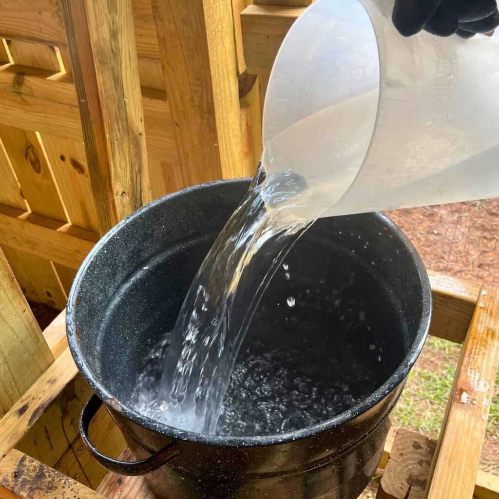 Woman pouring hot water into a large pot in an outdoor dairy barn.