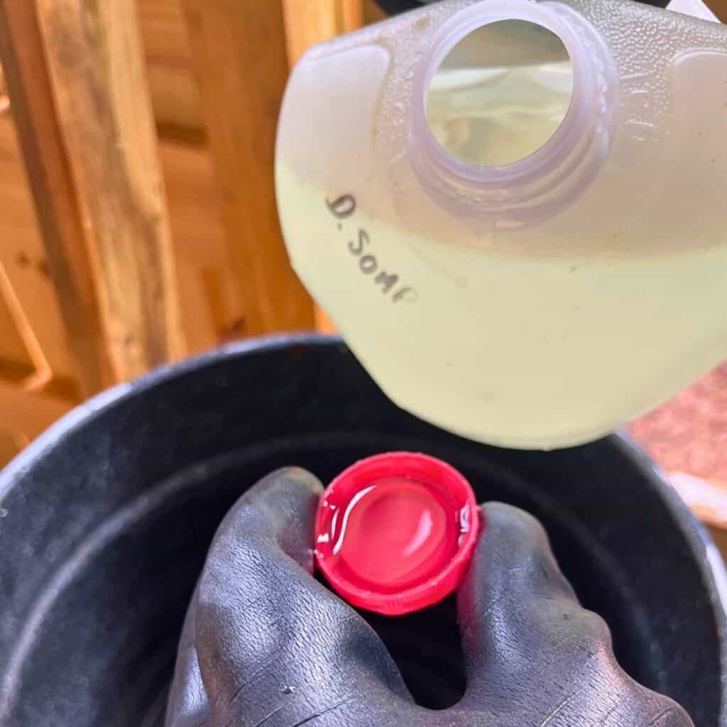 Woman pouring dairy soap into a cap over a pot of hot water inside a dairy barn.