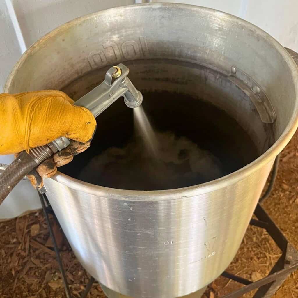 Woman filling up a large turkey fryer pot with a garden hose sprayer.
