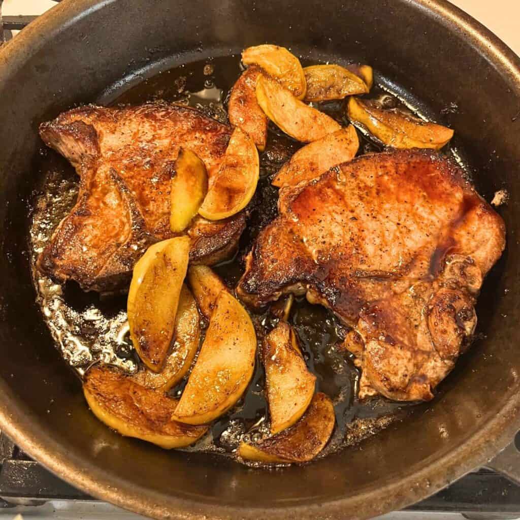 Two pork chops with caramelized apple slices in a cast iron skillet.