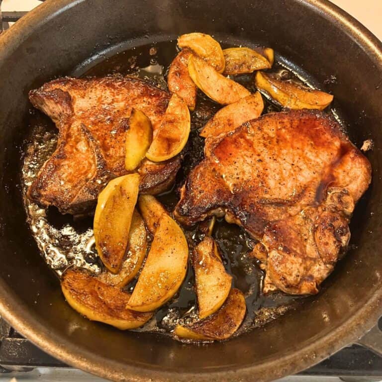 Two pork chops with caramelized apple slices in a cast iron skillet.