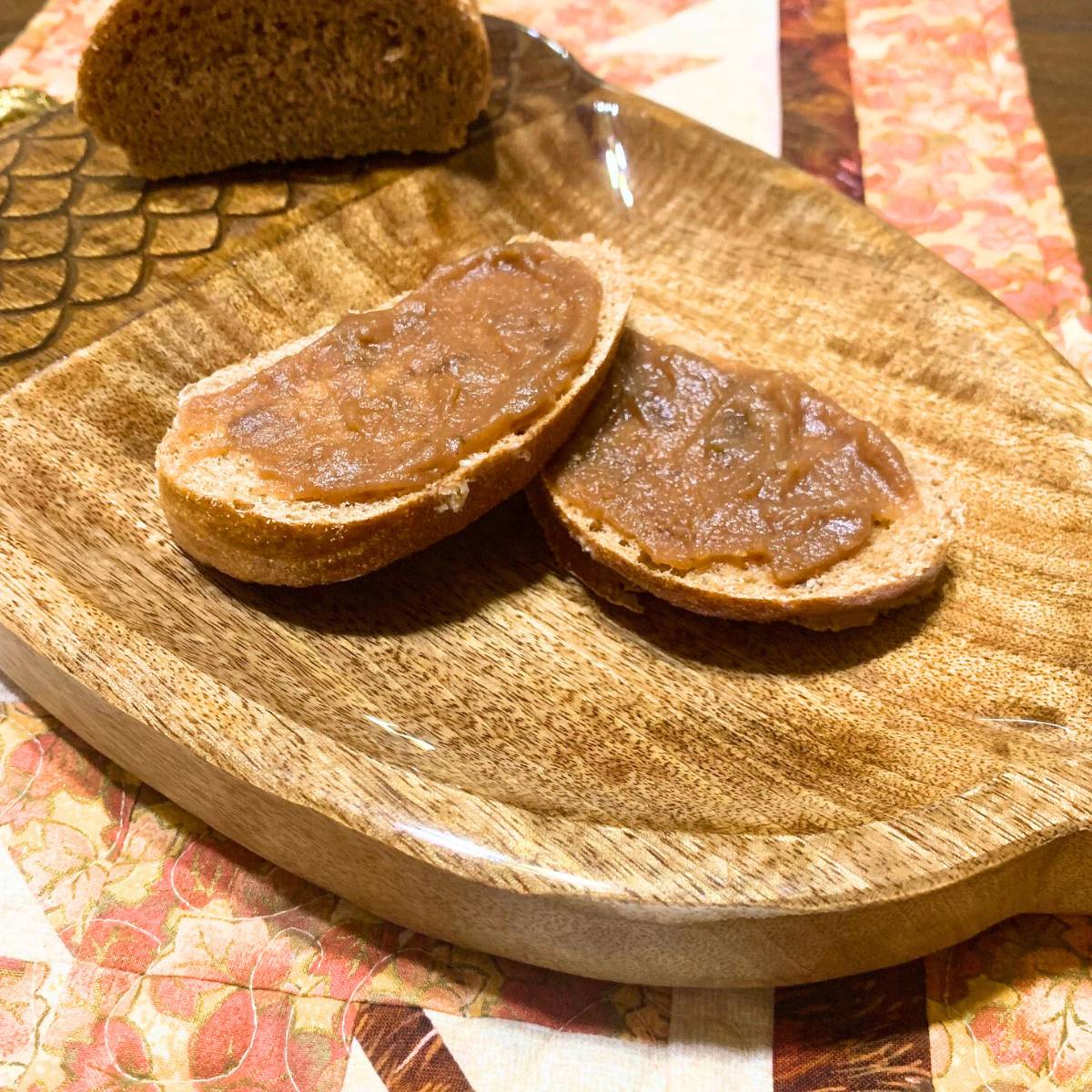 Two slices of homemade French bread slathered with homemade apple butter, sitting on a wood tray that looks like an acorn.