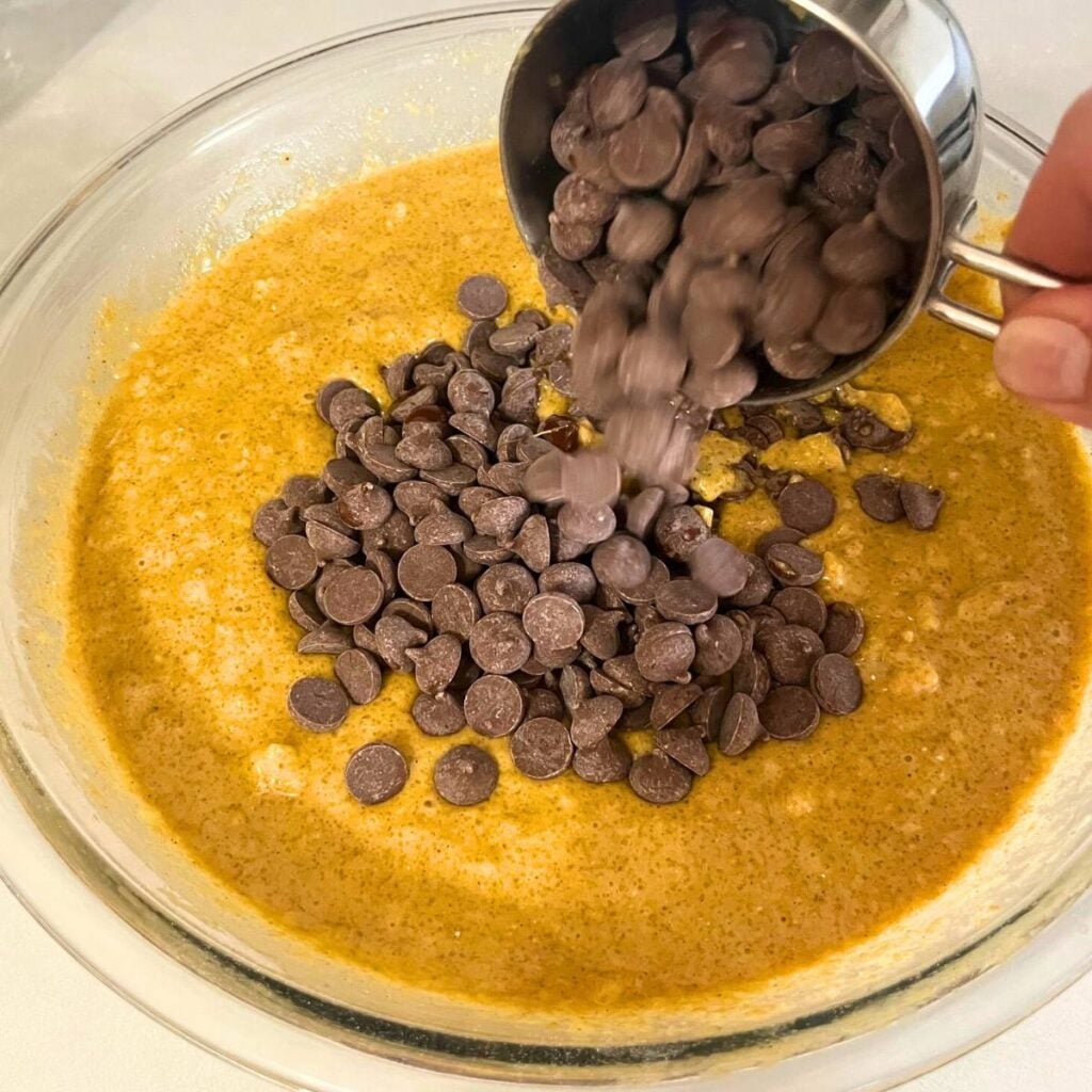 Woman adding chocolate chips to pumpkin bread batter.