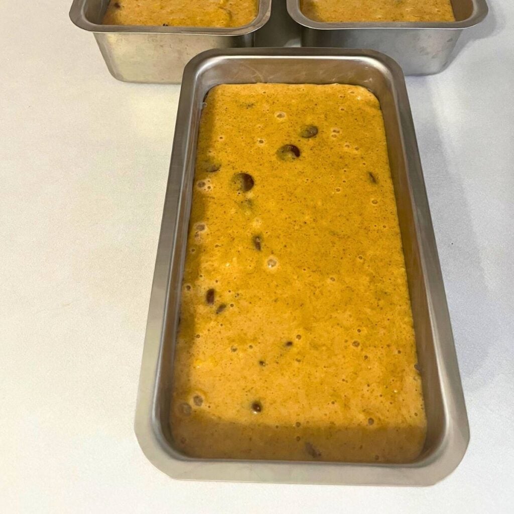 Chocolate chip pumpkin bread batter poured into a stainless steel loaf pan, sitting on a kitchen counter.