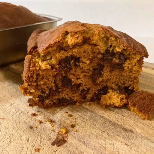 A slice of chocolate chip pumpkin bread sitting on a wood cutting board.
