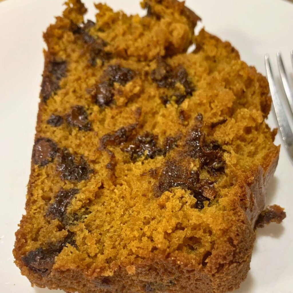 A slice of chocolate chip pumpkin bread on a white plate next to a silver fork.